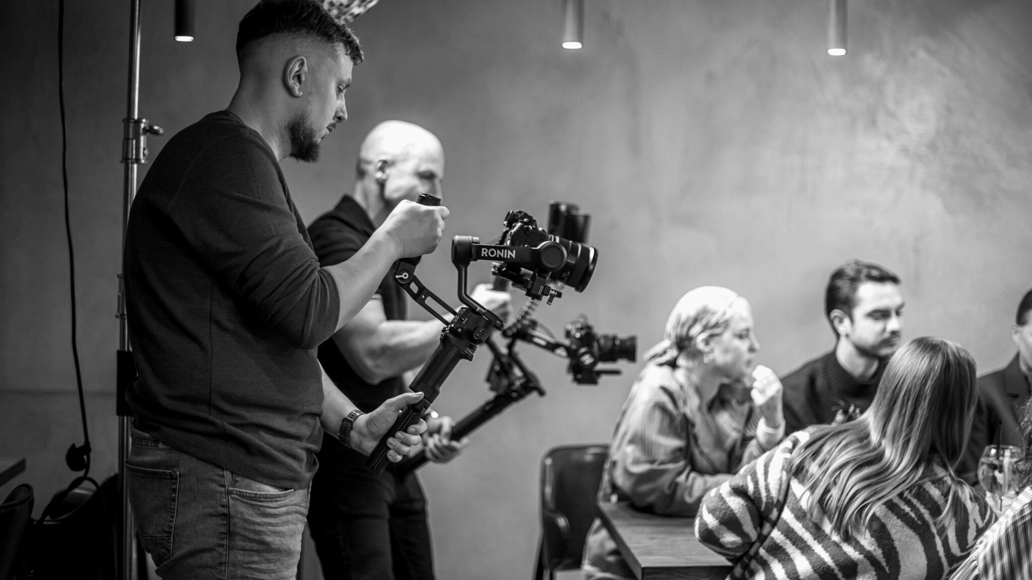 Du operatoriai su stabilizatoriais filmuoja žmones prie stalo – turinys socialiniams tinklams